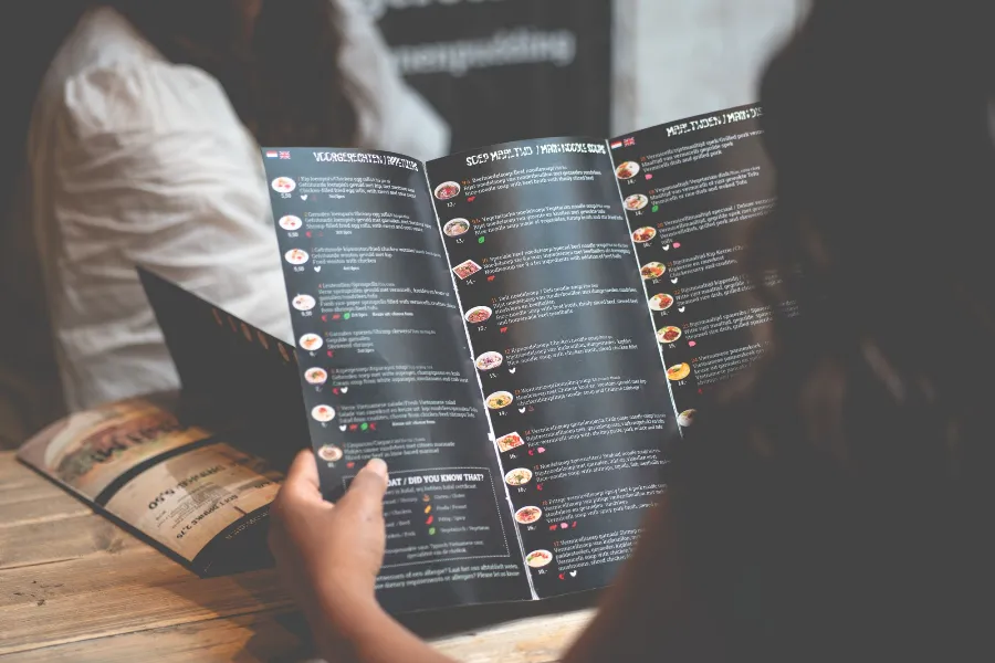 A guest reading a printed restaurant menu at a wooden table